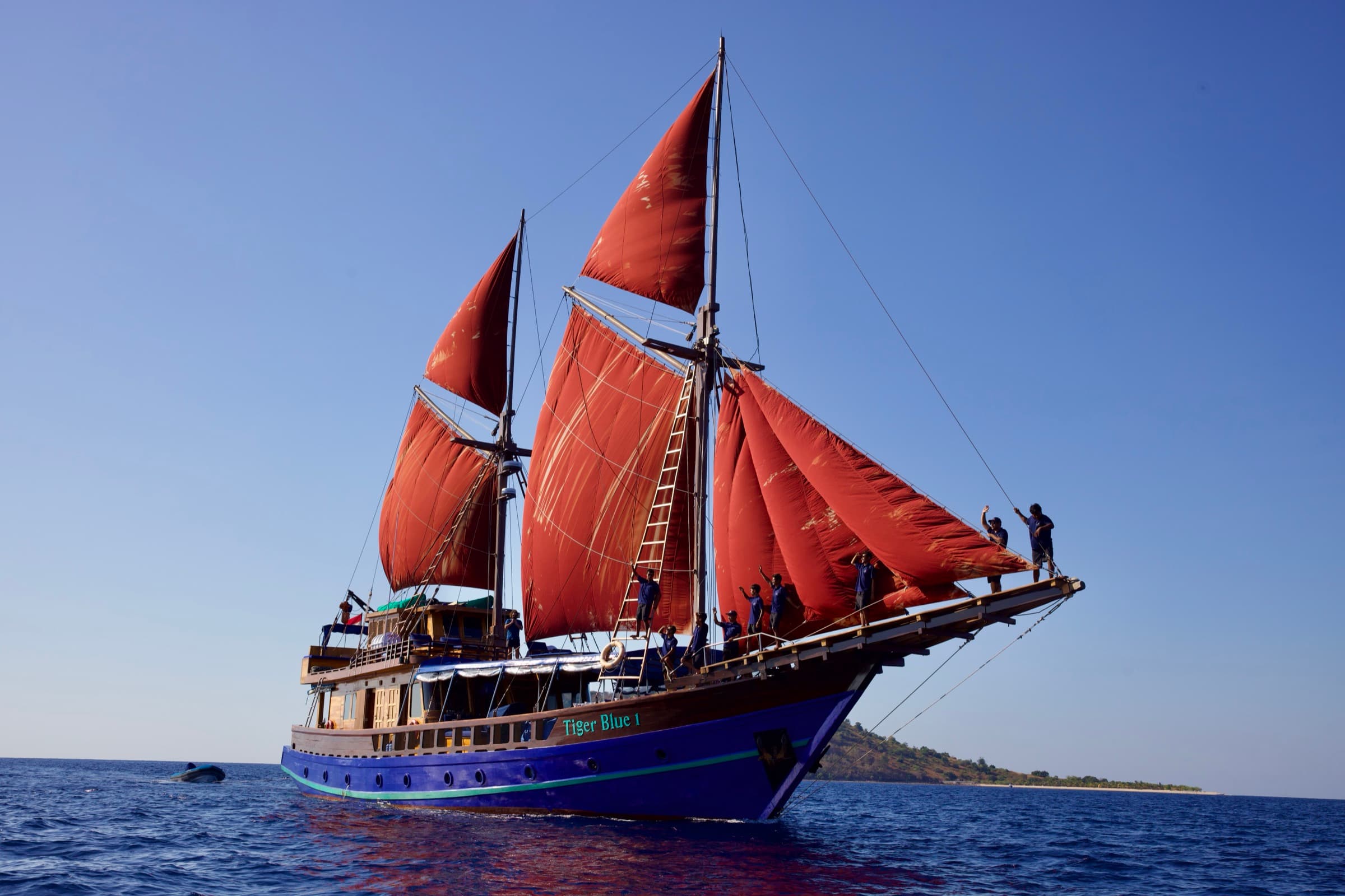 Tiger Blue under full red sail, blue water and islands behind